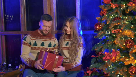 romantic couple with a gift. beautiful woman and handsome man holding big presents box at christmas time. lovely couple in knitted sweaters near christmas tree.