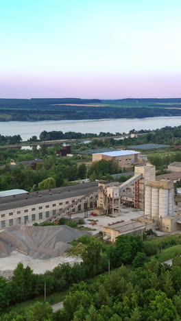 flying over green trees to industrial territory in summer. industrial factory near the river on the natural background. vertical video