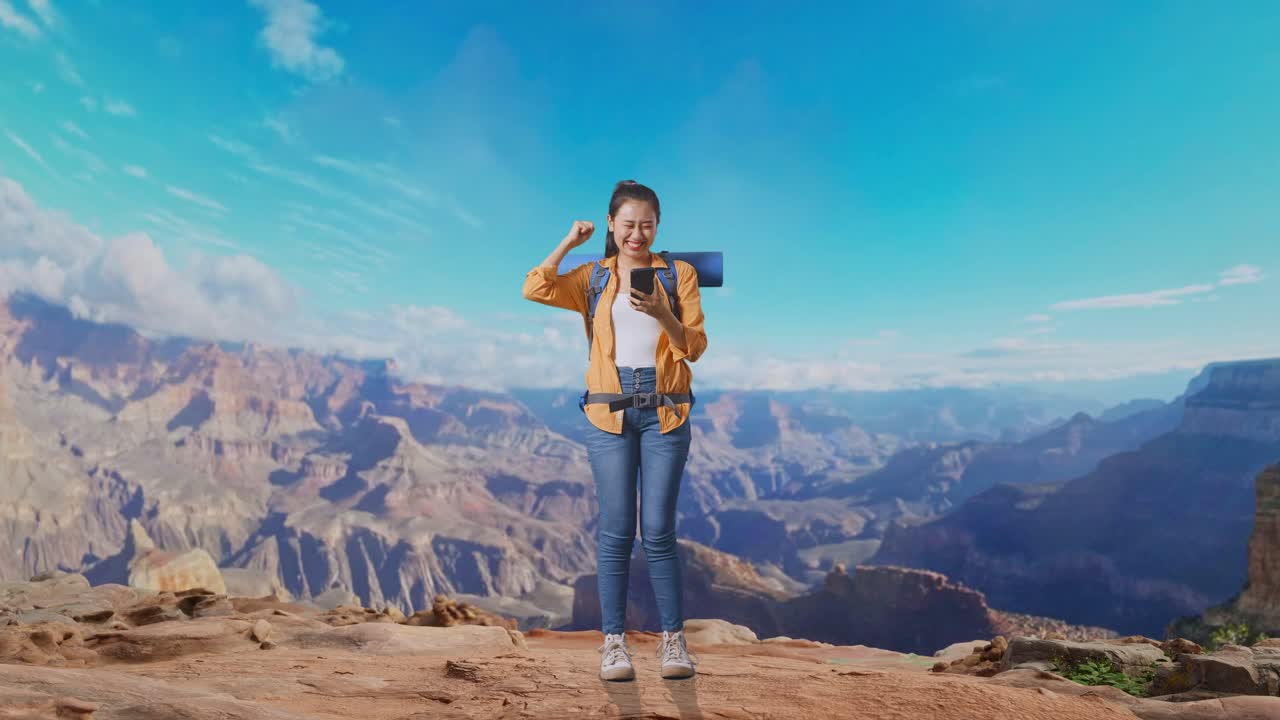 Full Body Of Asian Female Hiker With Mountaineering Backpack Looking At The Smartphone And Screaming Goal Celebrating The Success While Traveling At The Top Of Mountain