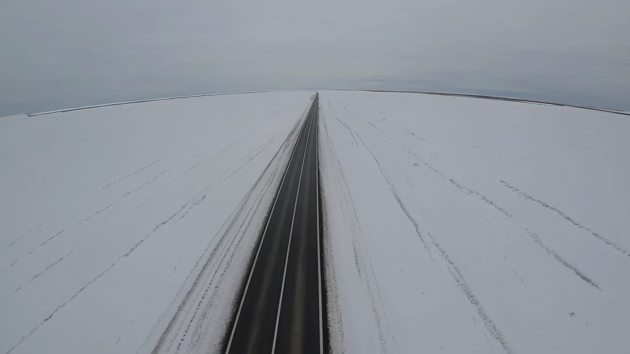 Aerial video of a long, straight road cutting through a vast, snow-covered landscape
