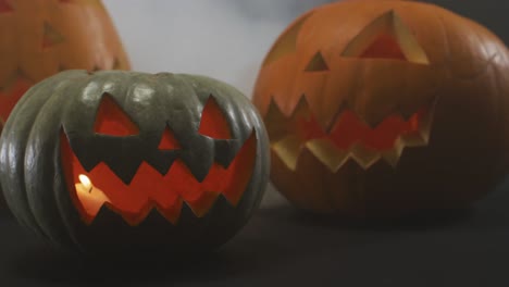 Raucheffekt-über-Mehreren-Gruseligen-Gesichtern-Geschnitzter-Halloween-Kürbis-Vor-Grauem-Hintergrund