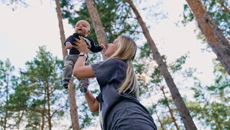woman holding her child over the head. loving mom kisses her little son and spinning in the nature backdrop. low angle view.