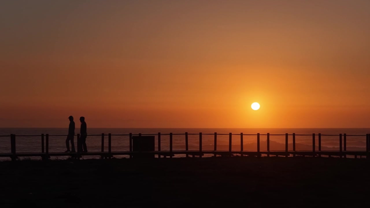 Drone shot of People walking at coastline during sunset. Cinematic silhouettes.