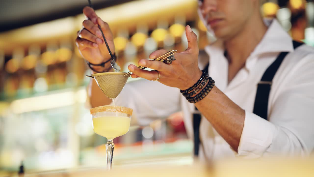 Barman professionista che filtra un cocktail in un bicchiere al bancone del bar