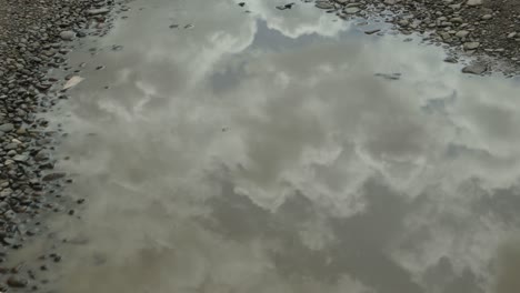 the sky, clouds and shadow of the walking woman are reflected in a big puddle