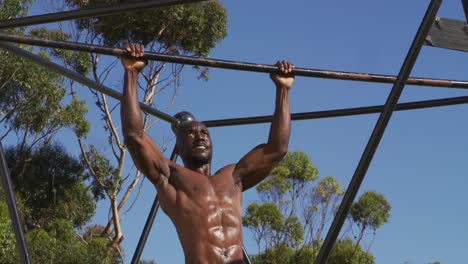 hombre afroamericano en forma, sin camisa haciendo ejercicio afuera, haciendo chin-upso en un marco de escalada