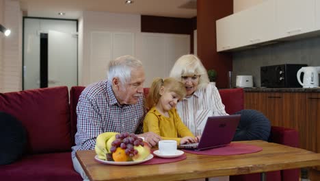 Pareja-Caucásica-Mayor-Con-Nieta-Niña-Usando-Una-Computadora-Portátil,-Viendo-Videos-Divertidos