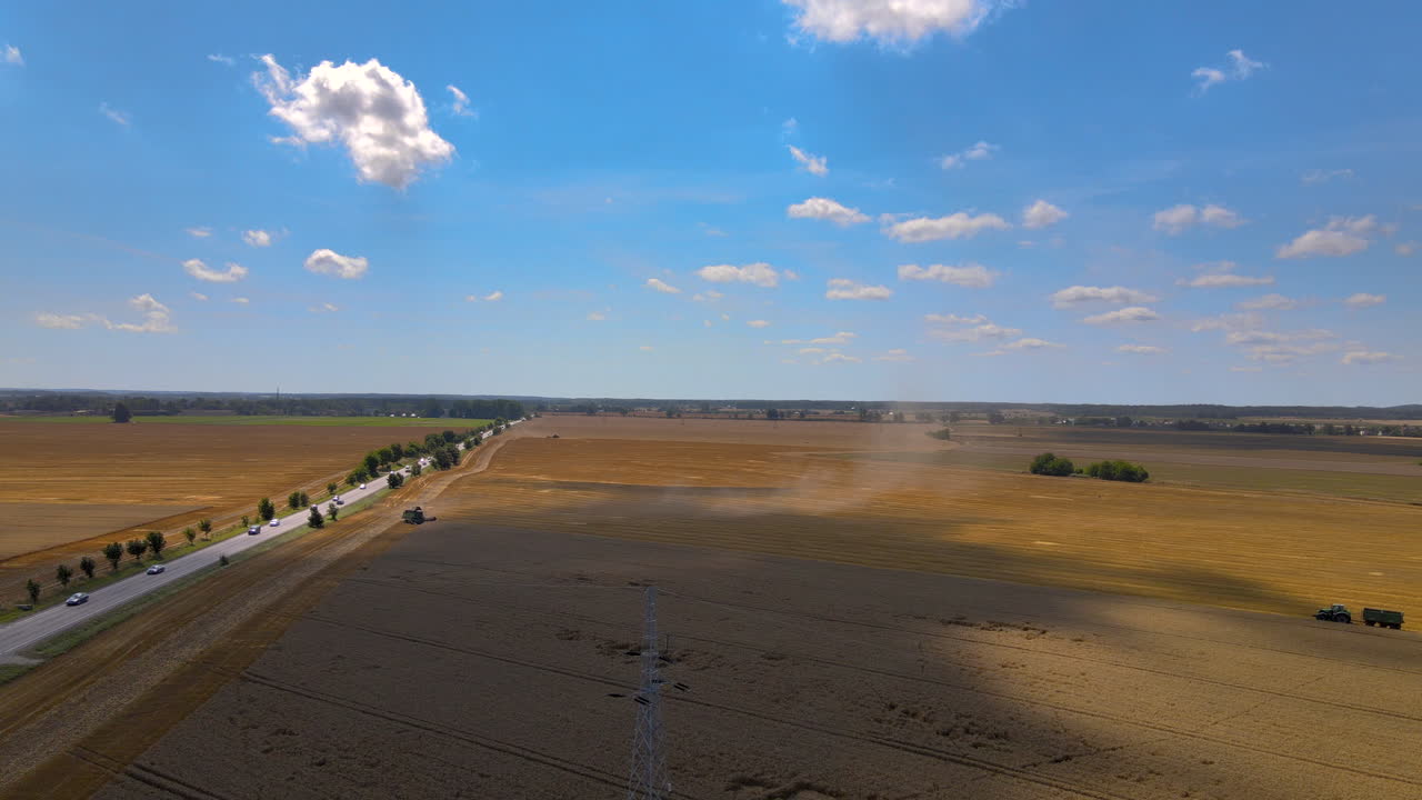Combine harvester mows the grain in the field, the agricultural machines work during the harvest season, beautiful weather outside, blue skies and gentle clouds, field near the roadway, aerial