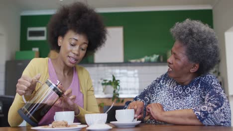 Happy-african-american-adult-daughter-and-senior-mother-talking-and-drinking-coffee,-slow-motion