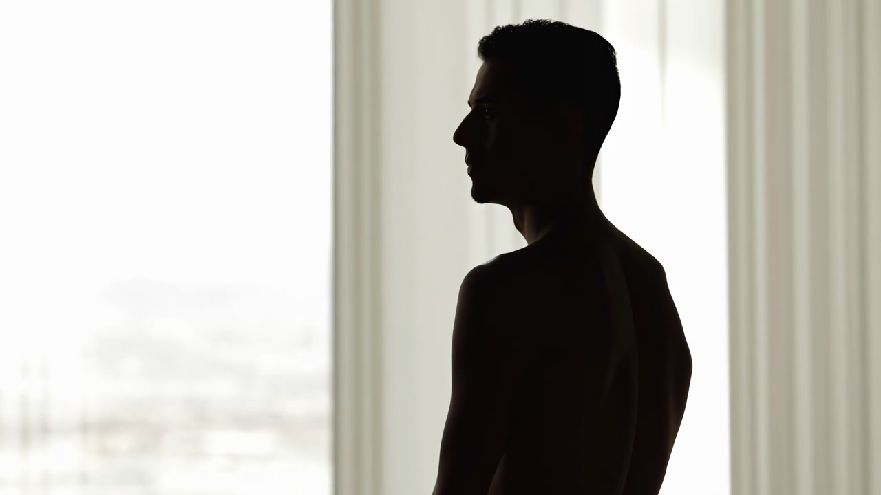 Perdeli pencerede ayakta duran adam, yandan profil görünümü. Siyah ve beyaz vurgularla nötr bir atmosferde, çevresindeki nesnelerle birlikte.