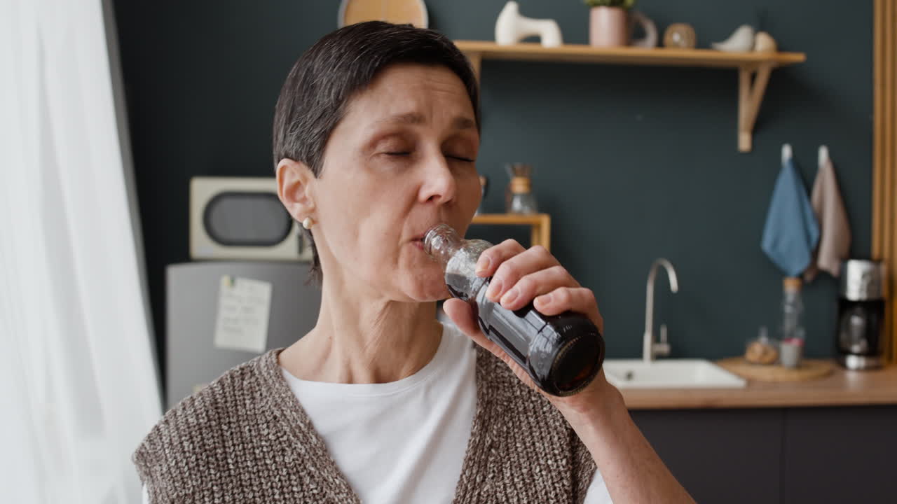 Mature Woman Drinking Beverage from a Bottle in Kitchen