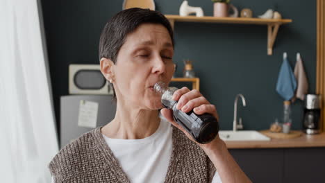 mature woman drinking beverage from a bottle in kitchen