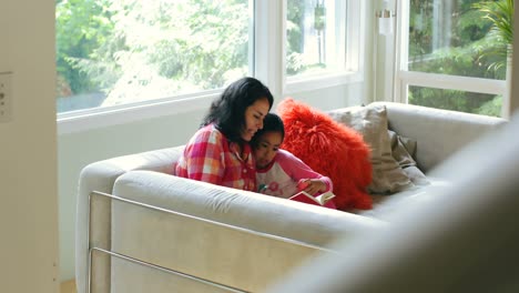 Madre-E-Hija-Leyendo-Un-Libro-En-La-Sala-De-Estar-4k