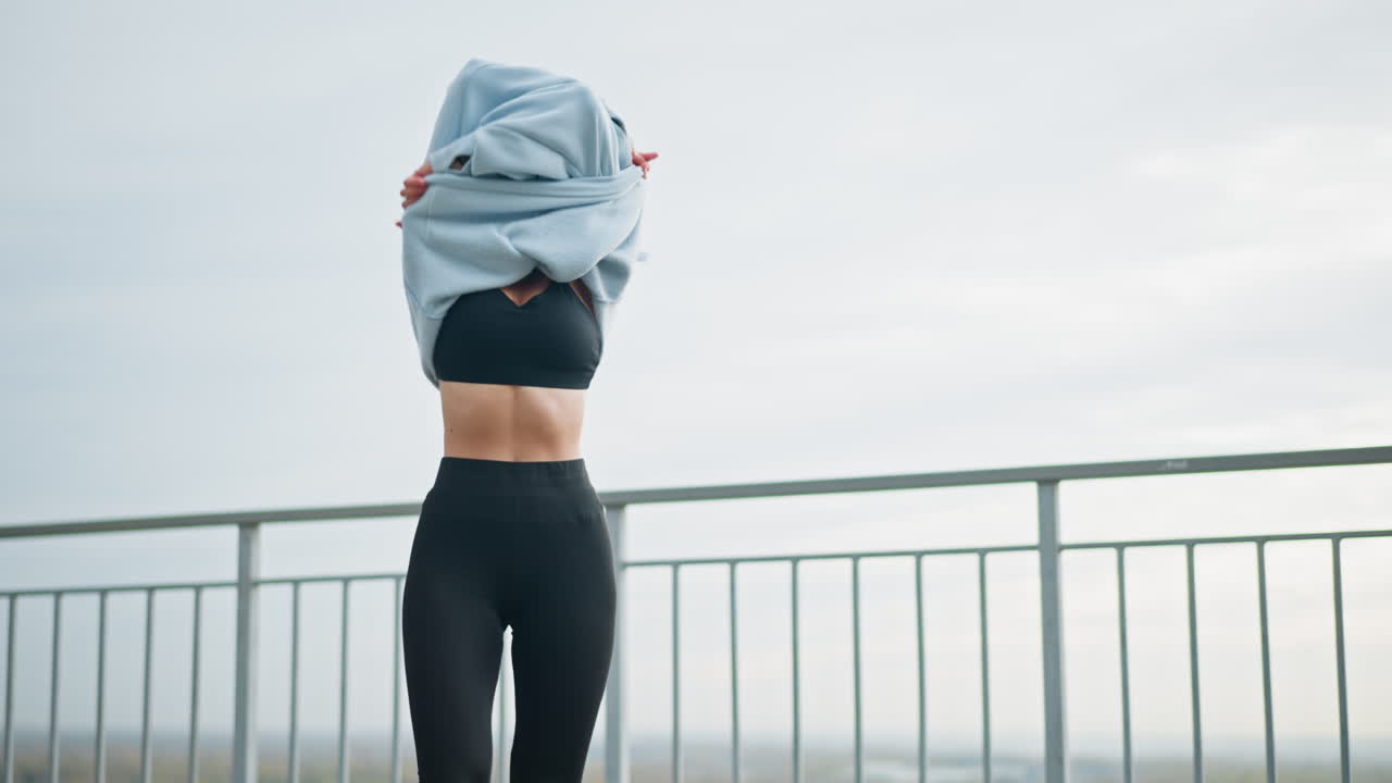 Pretty lady removing sweater, shaking her hair, and breathing deeply in outdoor setting with iron fence in background. Ideal for wellness, fitness, and relaxation moments