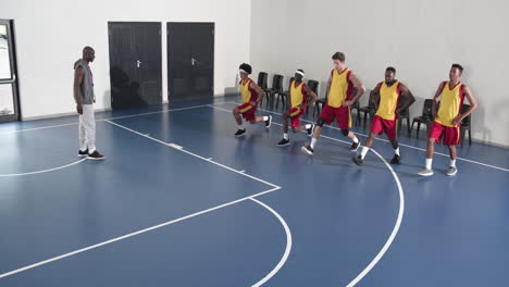 basketball players stretching on court with coach observing, preparing for practice