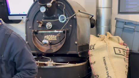 a coffee roasting machine operates in a cafe, surrounded by sacks of beans. warm lighting enhances the industrial setting