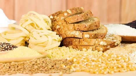 whole wheat bread, pasta, and grains arranged on a wooden background with warm lighting and static camera