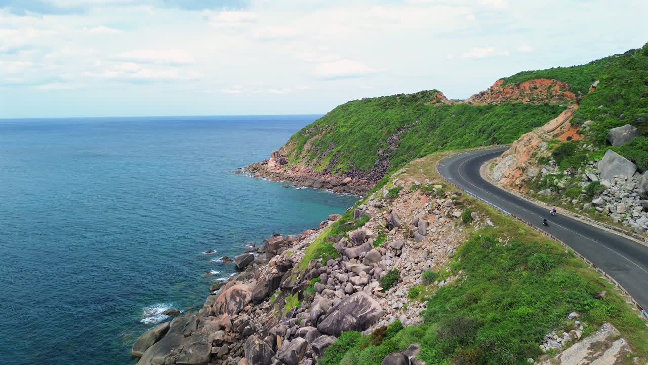 Aerial dolly of long Vietnamese coastline road above cliffs and turquoise sea, motorbikes drive