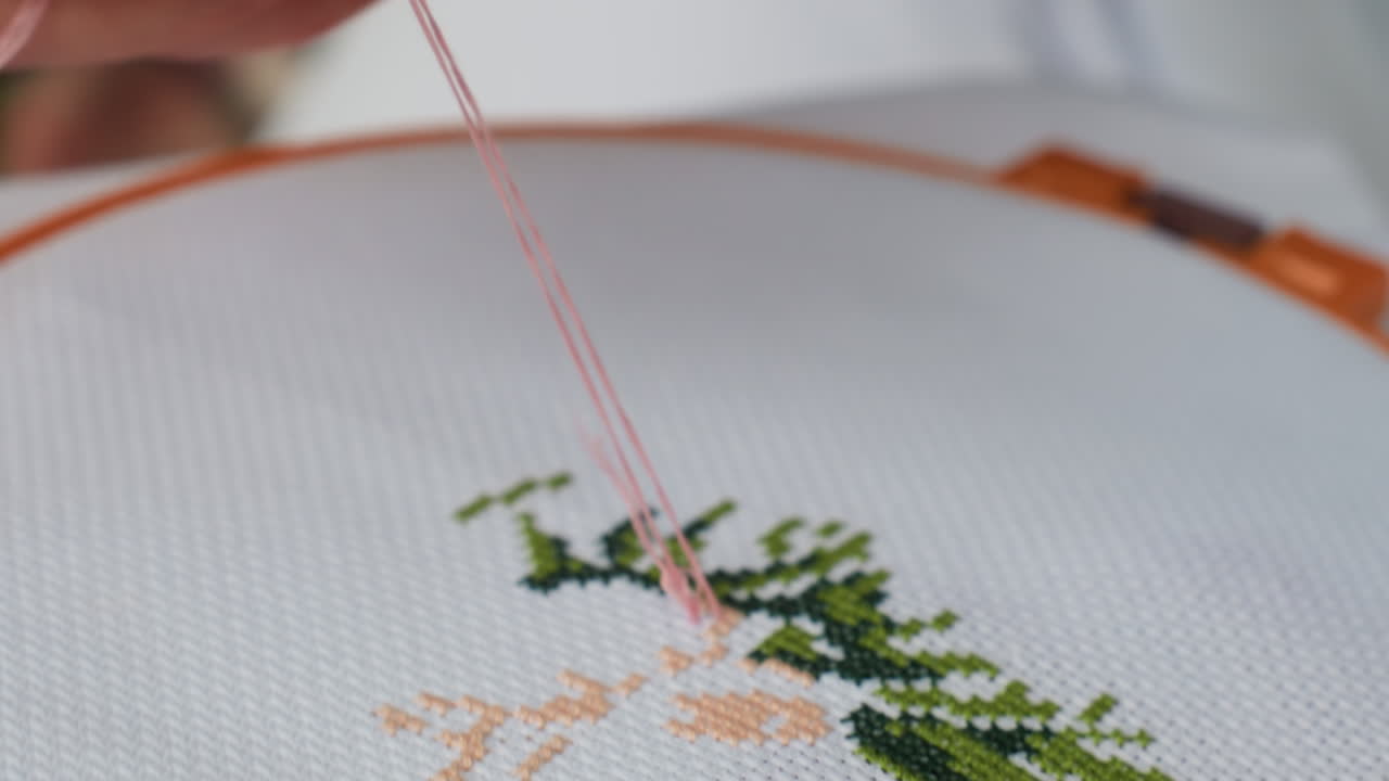 Close up of craft person embroidering green tree design on white fabric using pink thread, needle moving with precision, showcasing creativity, focus, and handmade artistry