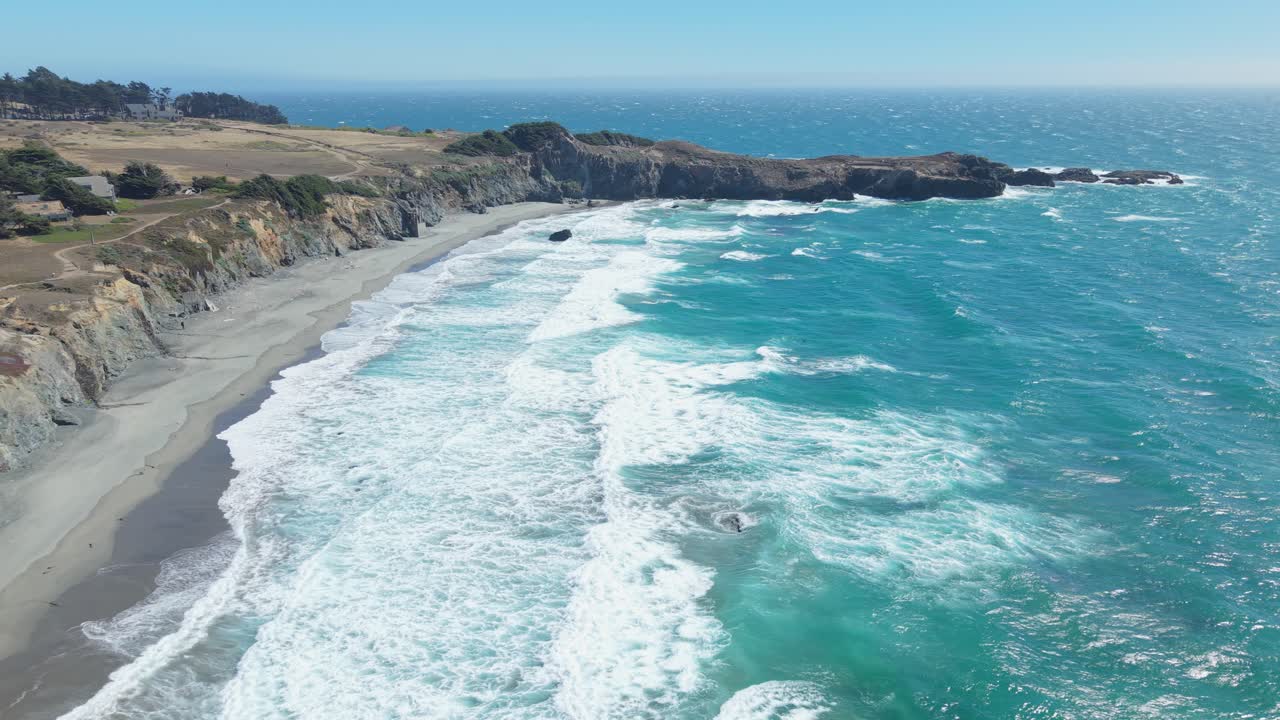 High-altitude drone footage showing California coastline with jetty, large waves, rocky shore, and cliffs during a slight backward movement over the ocean
