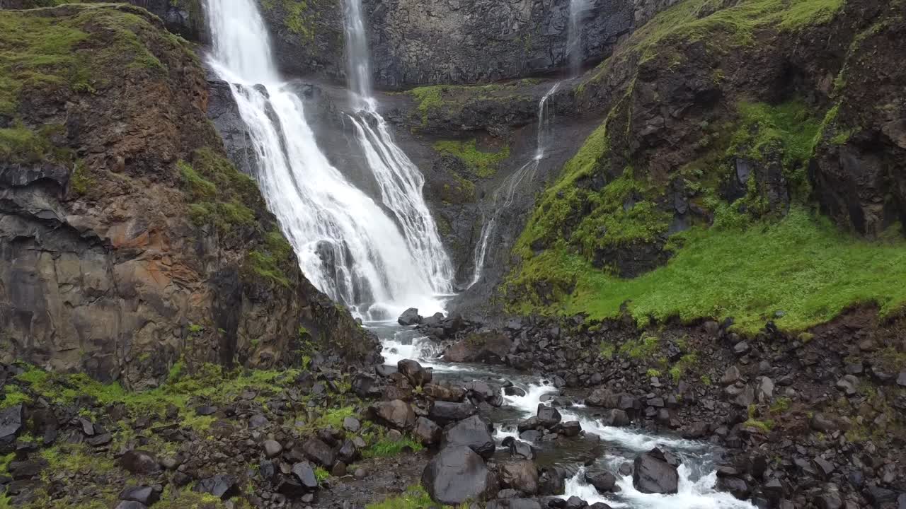 cascada glymur cayendo por un acantilado rocoso cubierto de musgo en islandia, vista aérea de drones