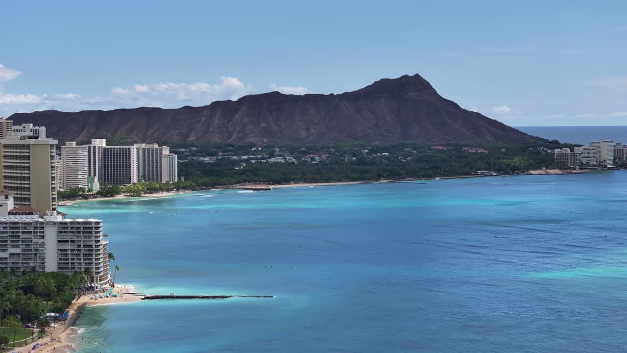 Aerial drone footage of Waikiki’s coastline in Honolulu, Oahu, Hawaii, showcasing the famous Diamond Head volcanic crater, turquoise ocean waters, palm trees, and tropical city skyline