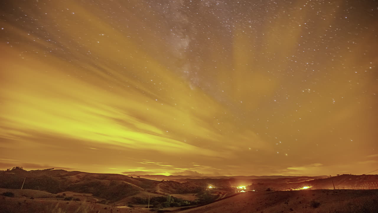 Stadlichter spiegeln sich in den Wolken, mit dem Kern der Milchstraße im Hintergrund – Astrofotografie-Zeitraffer.