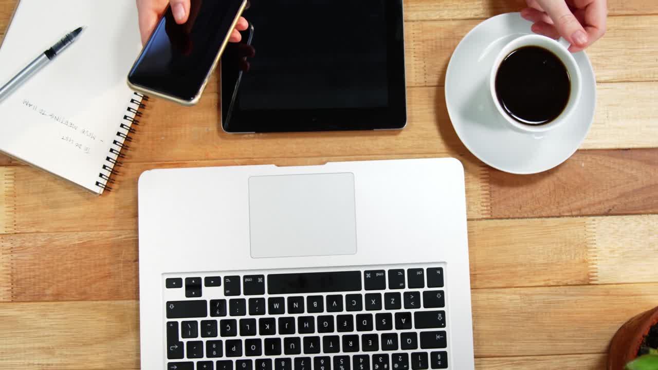 Hand of businesswoman using mobile phone at desk with coffee, laptop and digital tablet on table
