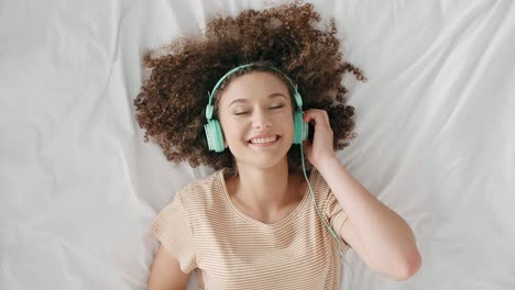 young woman lying on the bed and listening to music