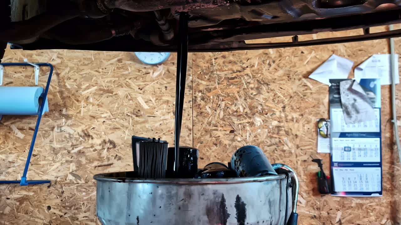 Dark engine oil drains from a vehicle into a catch pan, with an old filter ready for replacement