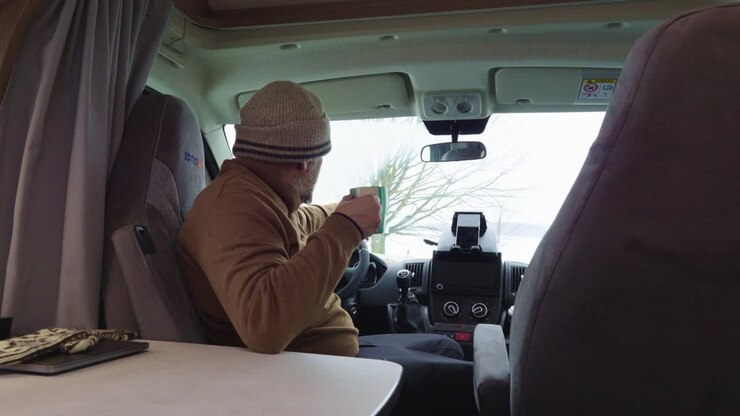Vista ravvicinata di un uomo anziano che beve caffè o tè in camper, in pausa dopo un lungo viaggio.