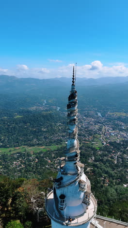approaching the stunning the ambuluwawa tower temple with tourists walking by the winding stairs. top view. aerial perspective on the green panorama of gampola town, sri lanka. vertical video.
