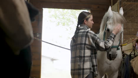 mujer joven acariciando caballo blanco en el establo