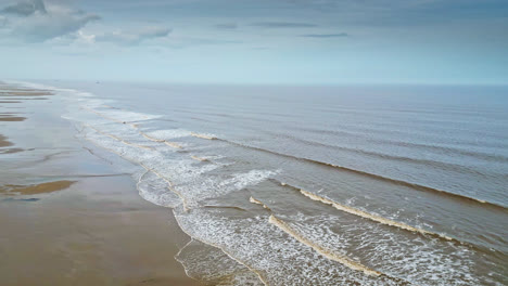 aerial video footage of a coastal beach scene with ocean, sand dunes and crashing waves