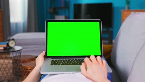 man working on green mock-up screen laptop computer. guy using laptop device, browsing internet, watching content, videos. point of view camera shot