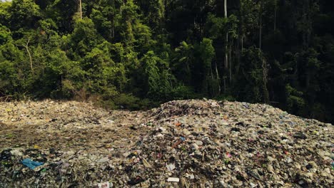 aerial ascending footage of land fill garbage dump with birds flying towards camera in jungle in the tropics in thailand