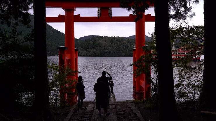 Folle di turisti che scattano foto al Santuario di Hakone con una nave pirata che transita sullo sfondo.