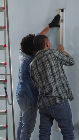 african-american constructors check wall with spirit level working in studio backside view. black men builders in casual clothes repair home. house renovation