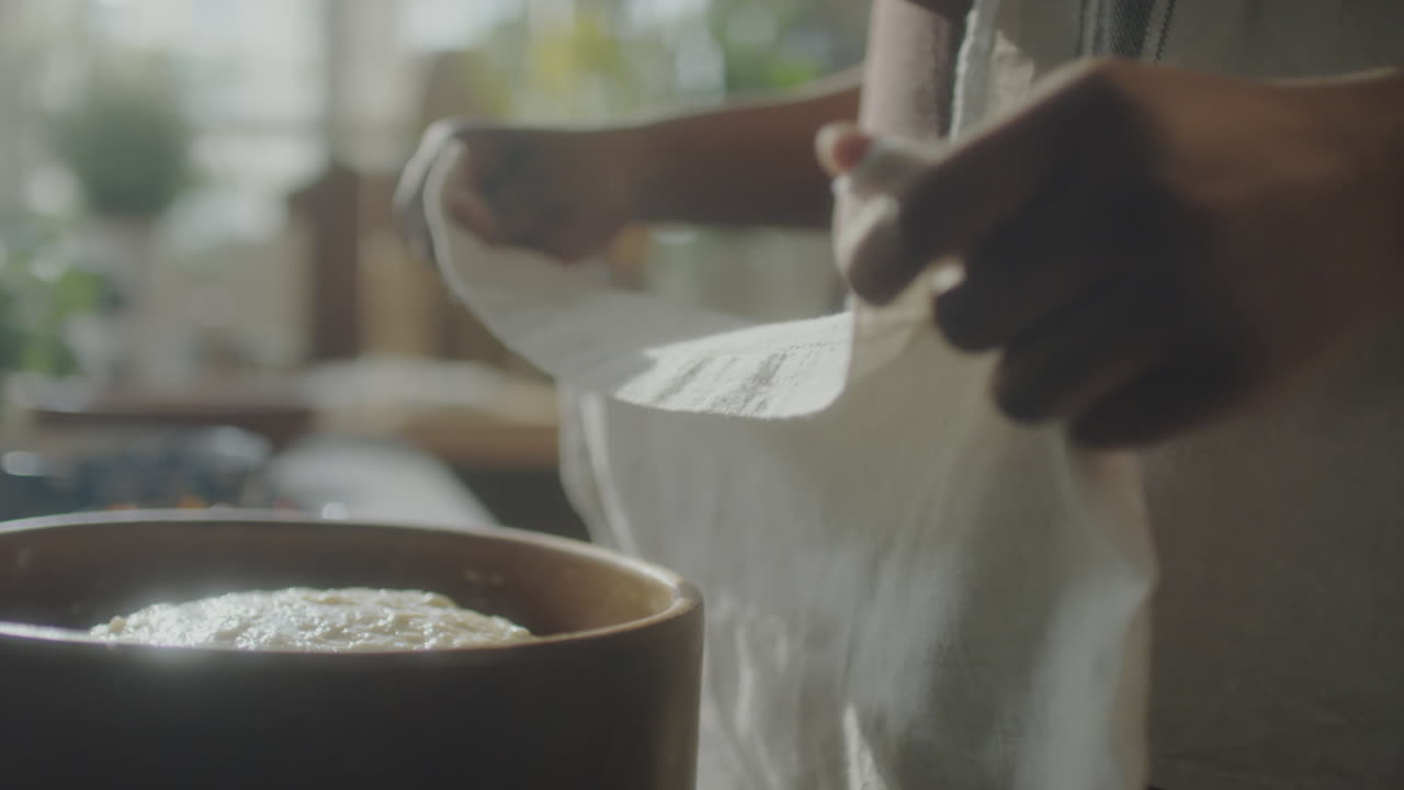 Hands covering a bowl of dough with a cloth