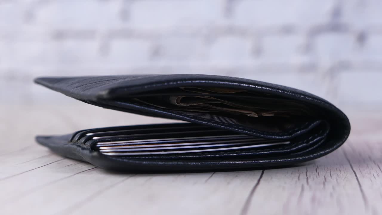 Open black leather wallet with credit cards and cash on a wooden surface