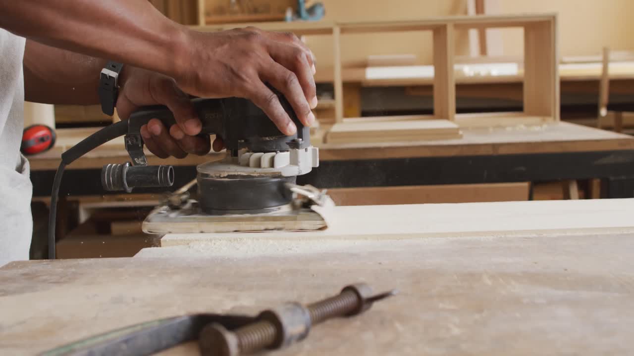 Close up of african american male carpenter hand's using an electric grinder to grind wooden plank