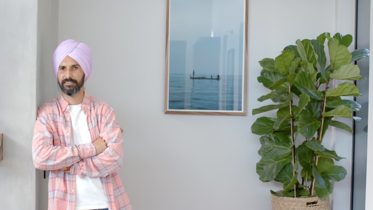 Står med krydsede arme, mand i turban smiler nær stueplante derhjemme