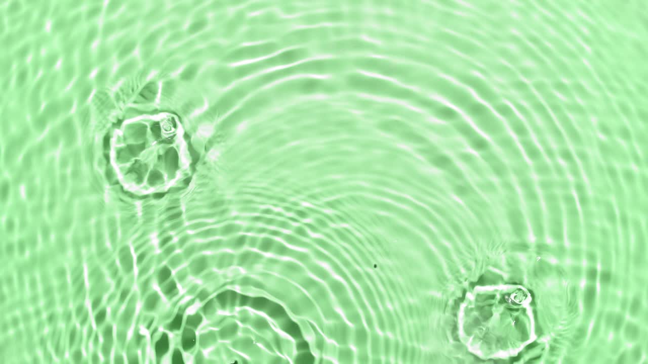 A lot of clear drops fall down on water surface creating circles