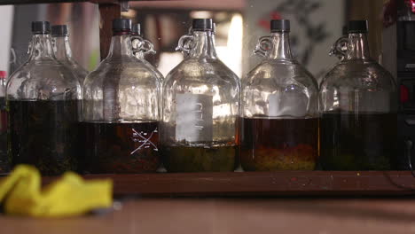 a group of homemade bottles of liquor infusing with different herbs sitting on a bar