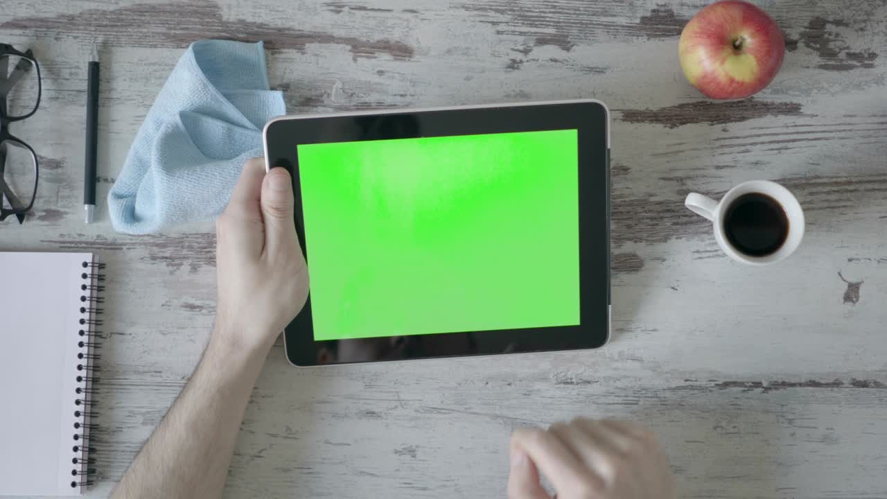 Hænder holder tablet-pc med grøn tom skærm på træbaggrund.