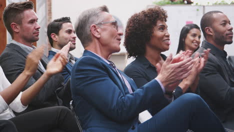 group of businessmen and businesswomen applauding presentation at conference