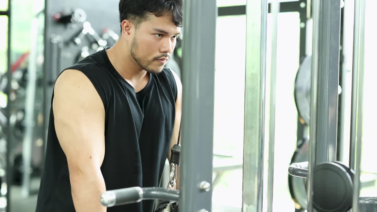 Focused man performs triceps cable rope exercise in bright Bangkok gym, showcasing strength and determination