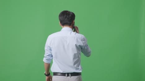 스튜디오에서 녹색 화면 배경에서 는 동안 휴대 전화로 이야기하는 아시아 사업가의 뒷면
