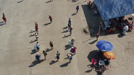 Bird's-eye-aerial-drone-shot-of-a-marching-band-and-teens-dressed-as-furry-bears-performing-and-asking-for-money-for-Carnaval-on-the-tropical-Bessa-beach-in-Joao-Pessoa,-Paraiba,-Brazil