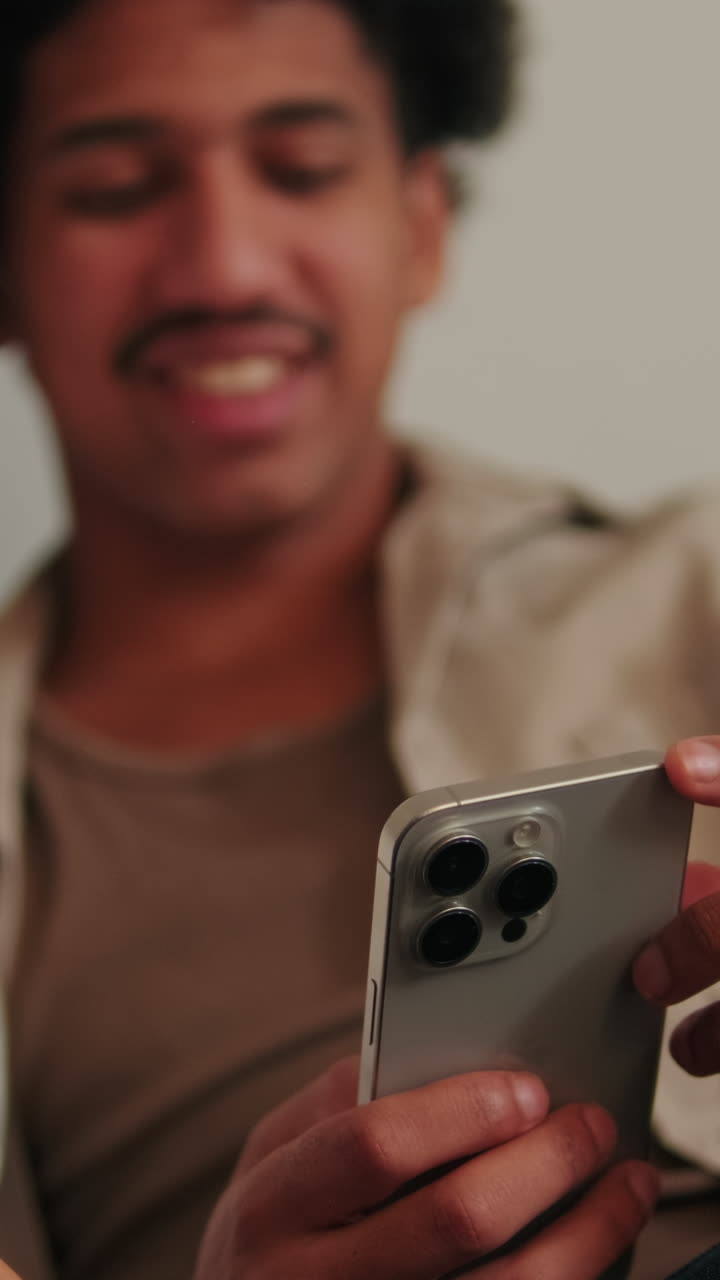 Giovane uomo che sorride mentre tiene in mano e guarda lo smartphone